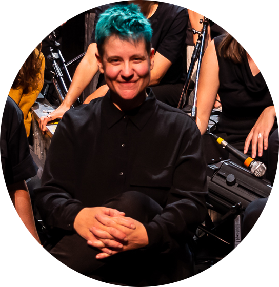 Jade, habillé.e de noir et cheveux turquoise, sourit.